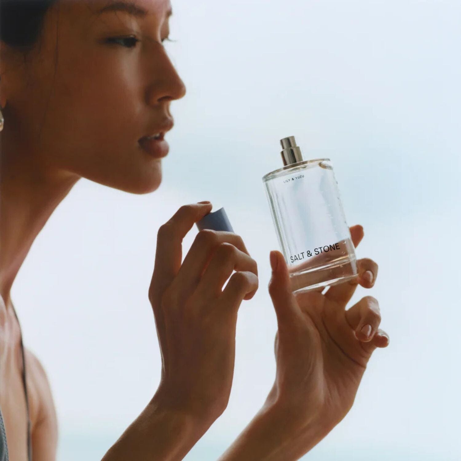 Woman smelling the Lily & Yuzu body mist by Salt & Stone on a light blue background