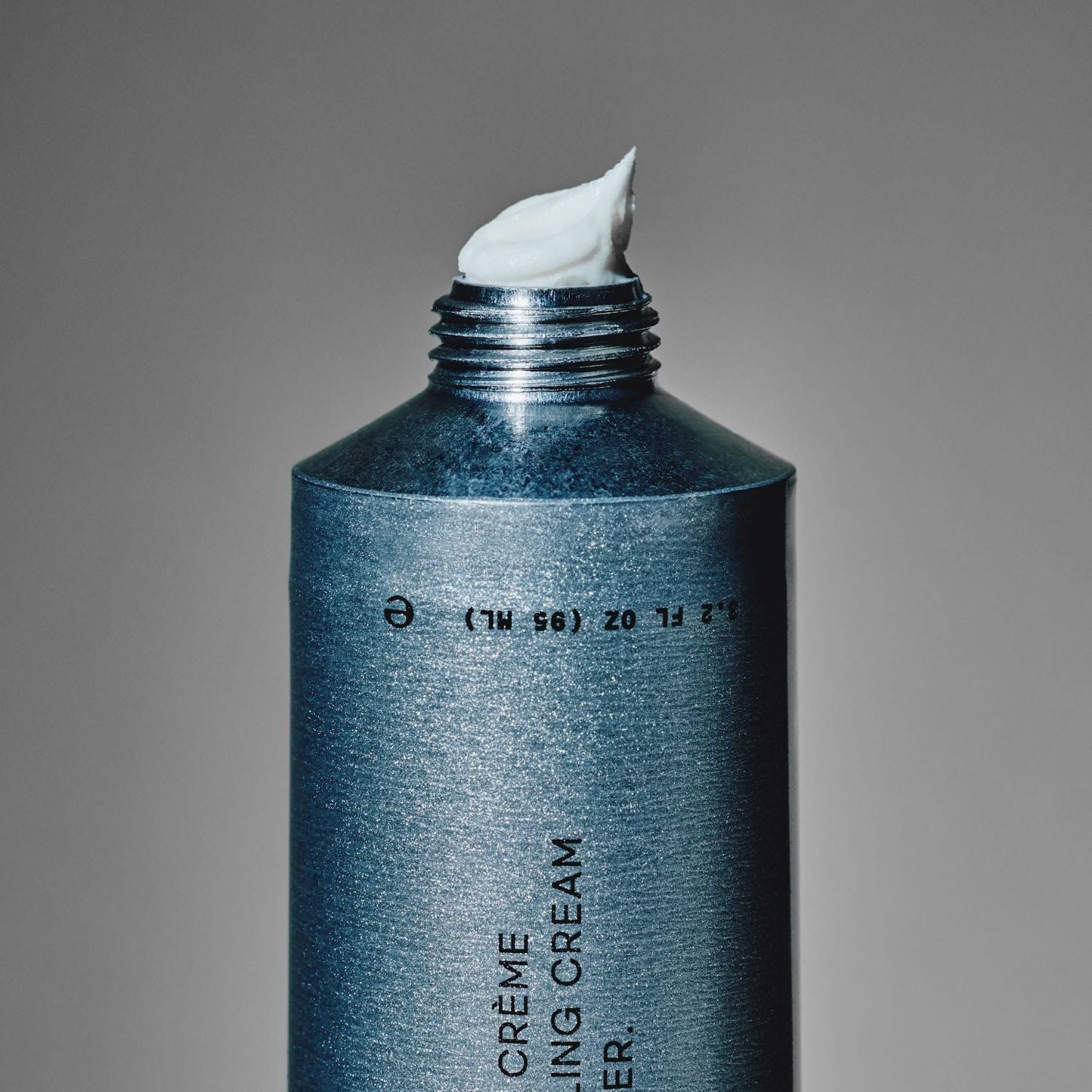 Silver tube of hair cream with a white cream coming out on a gray background