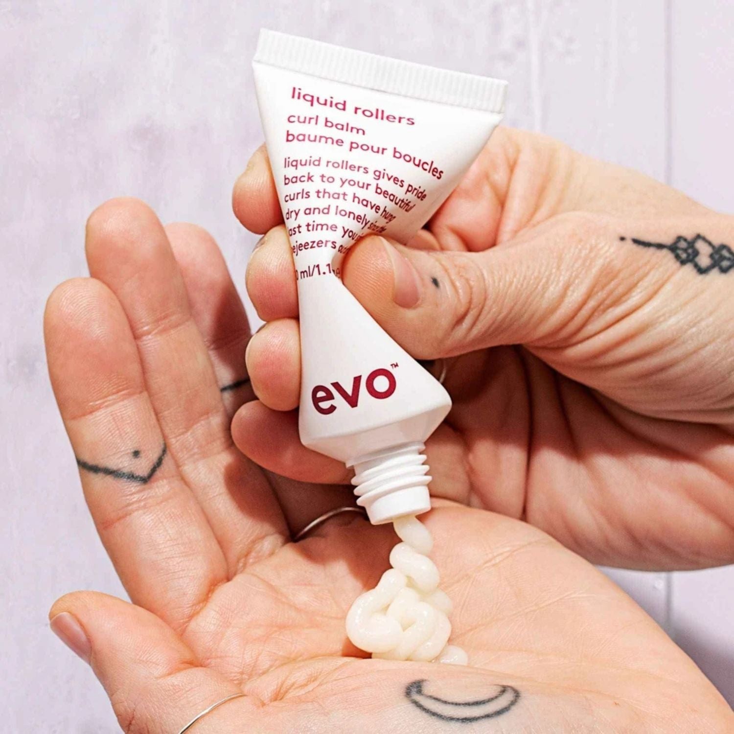 Tube of evo liquid rollers curl balm being squeezed onto a hand with visible tattoos.