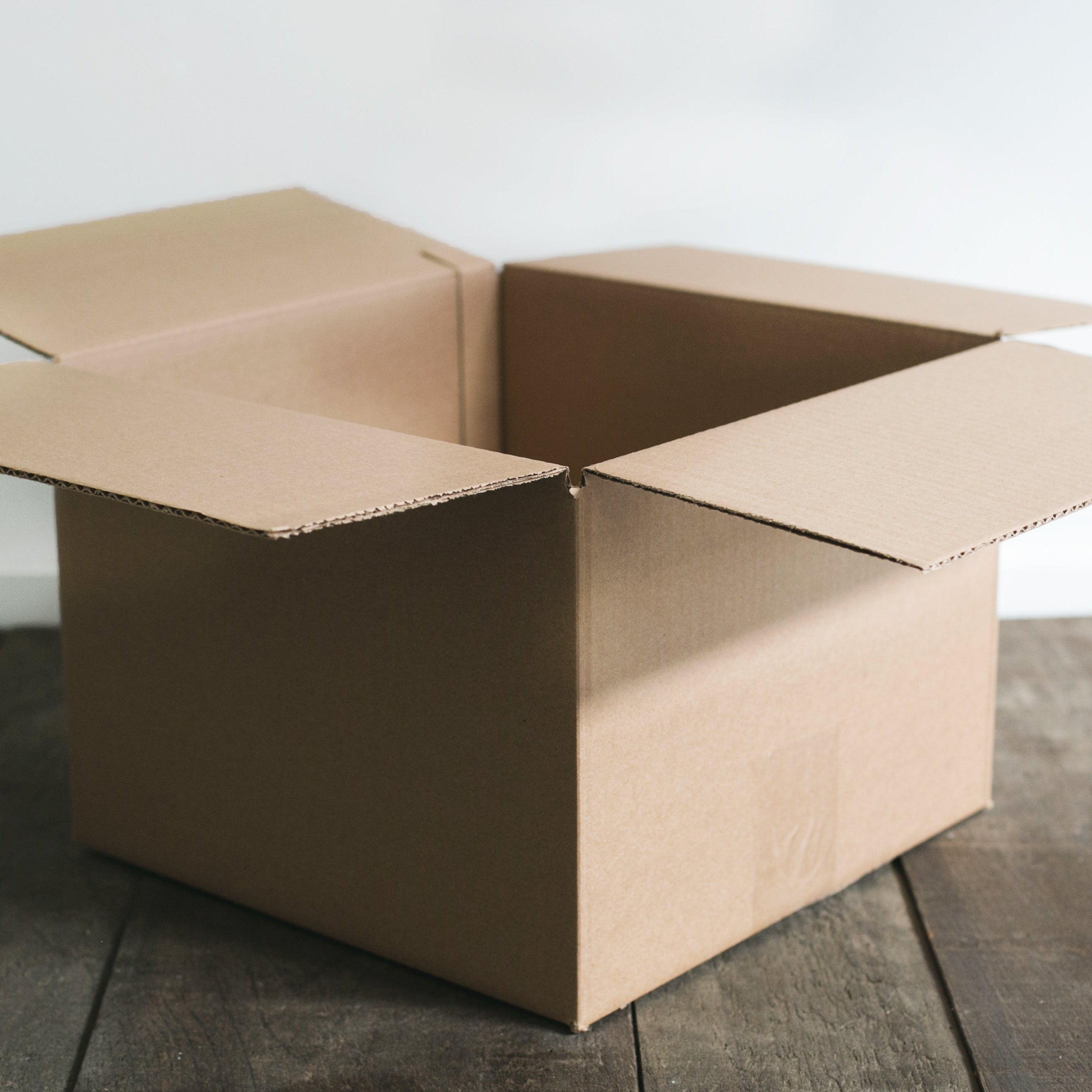 Open cardboard box on a wooden floor with a white wall background