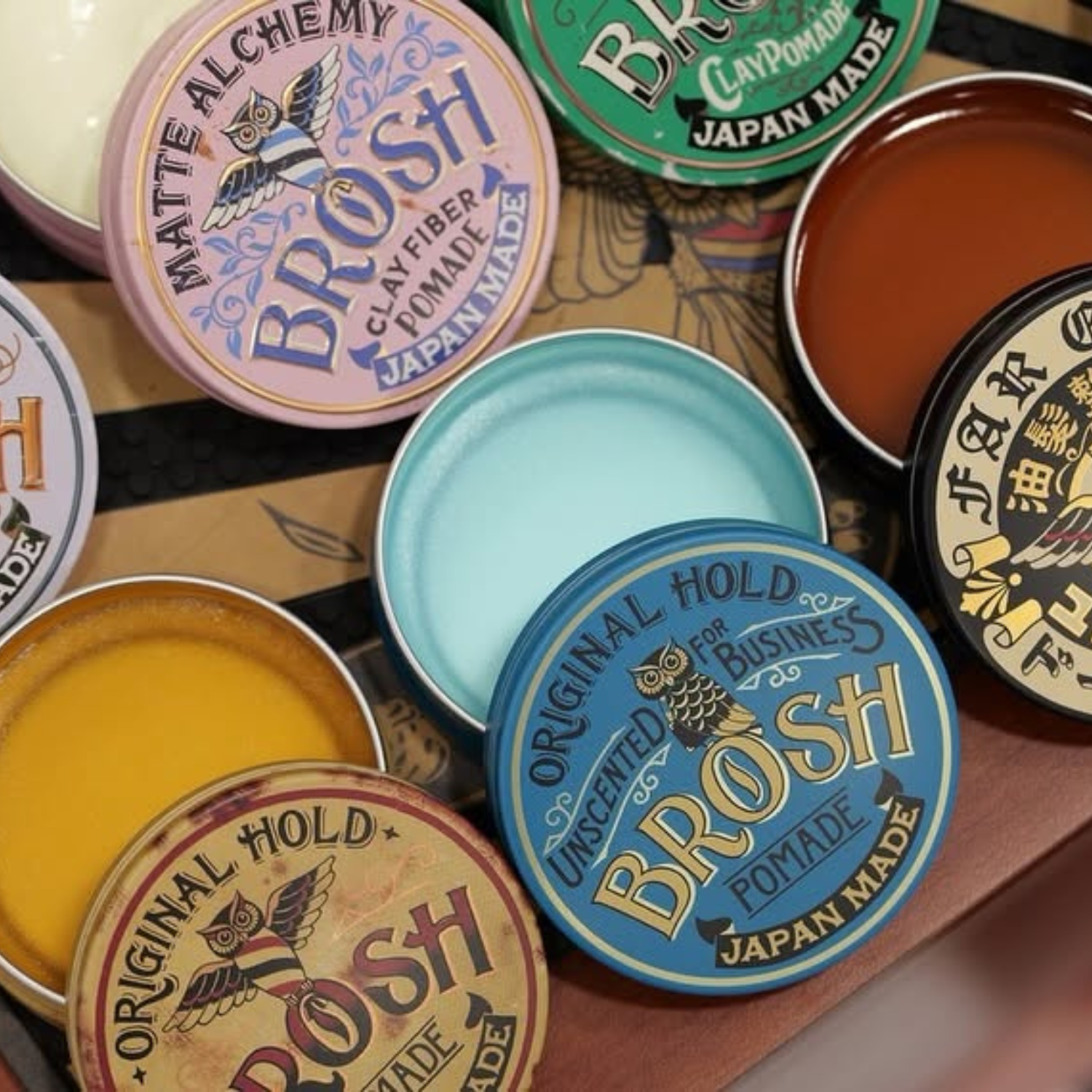collection of brosh pomades with the lids off on a wooden surface.