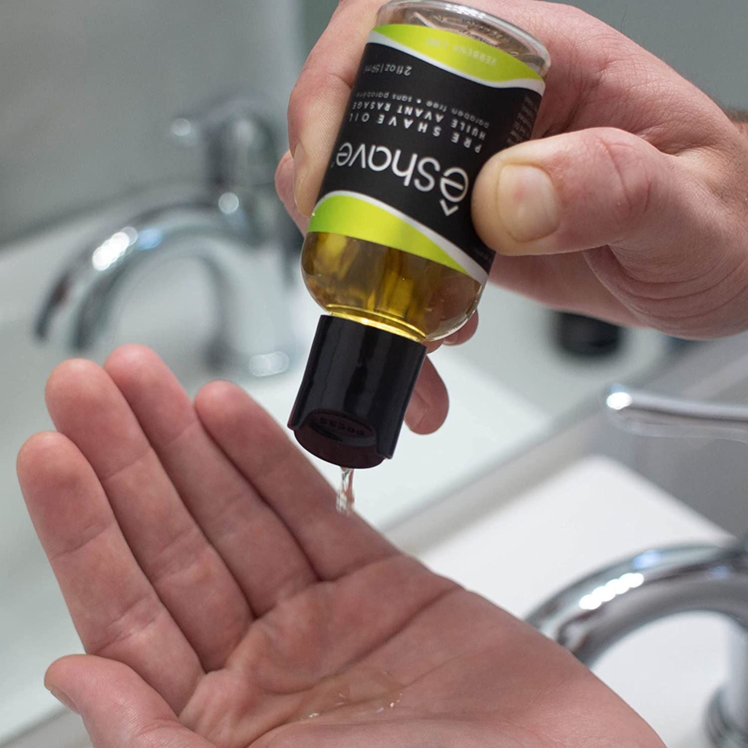 Hand holding a bottle of Shaving Company product with liquid dripping into another hand over a sink.