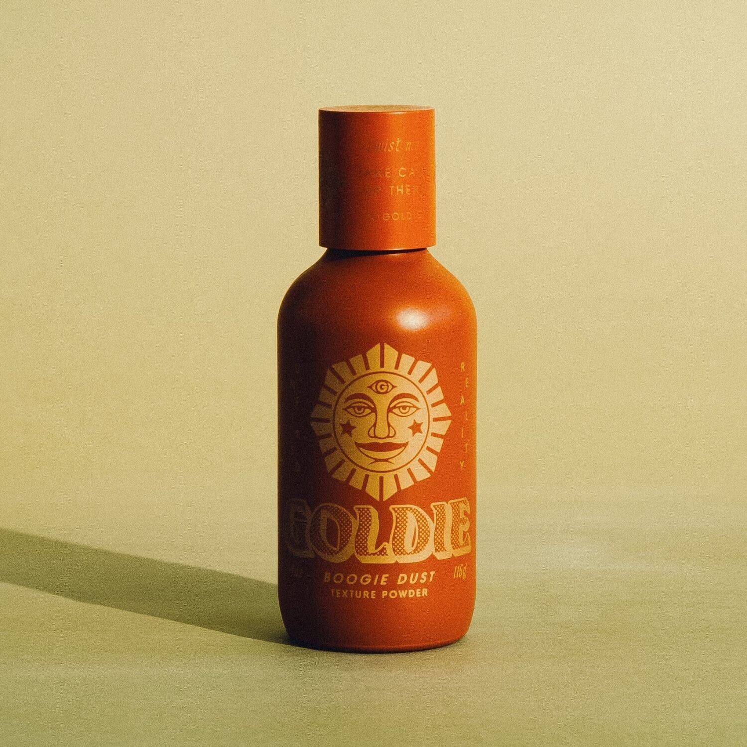 Orange bottle with sun design and 'Goldie' branding on a beige background