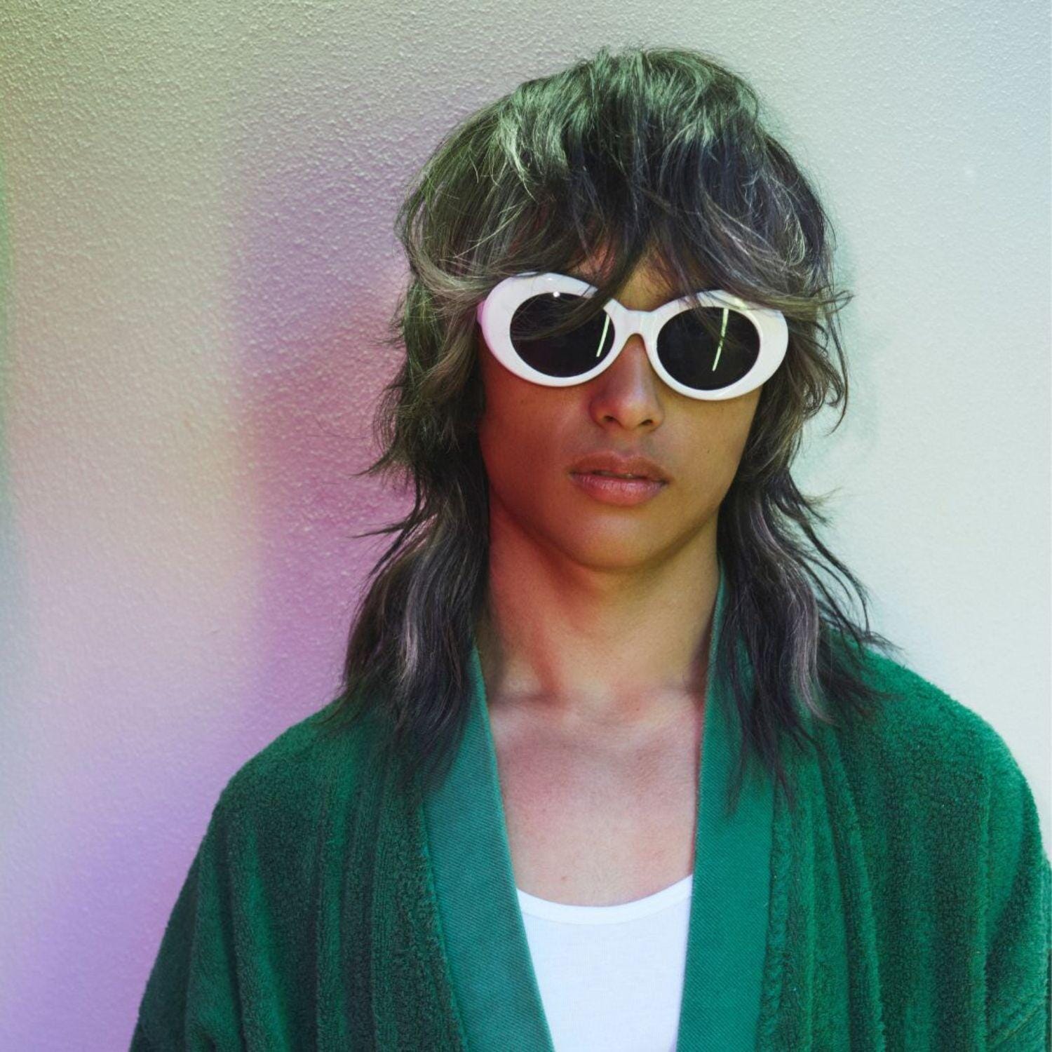 Man with long textured hair wearing white sunglasses and a green sweater