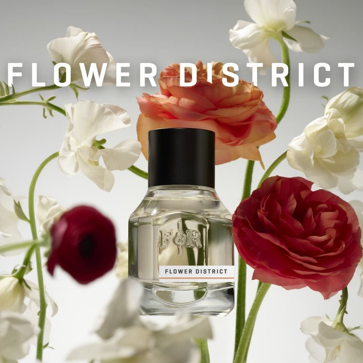A clear glass perfume bottle labeled FLOWER DISTRICT with a black cap, centered among large white, peach, and deep red flowers on a light gray background. The words FLOWER DISTRICT appear across the top.
