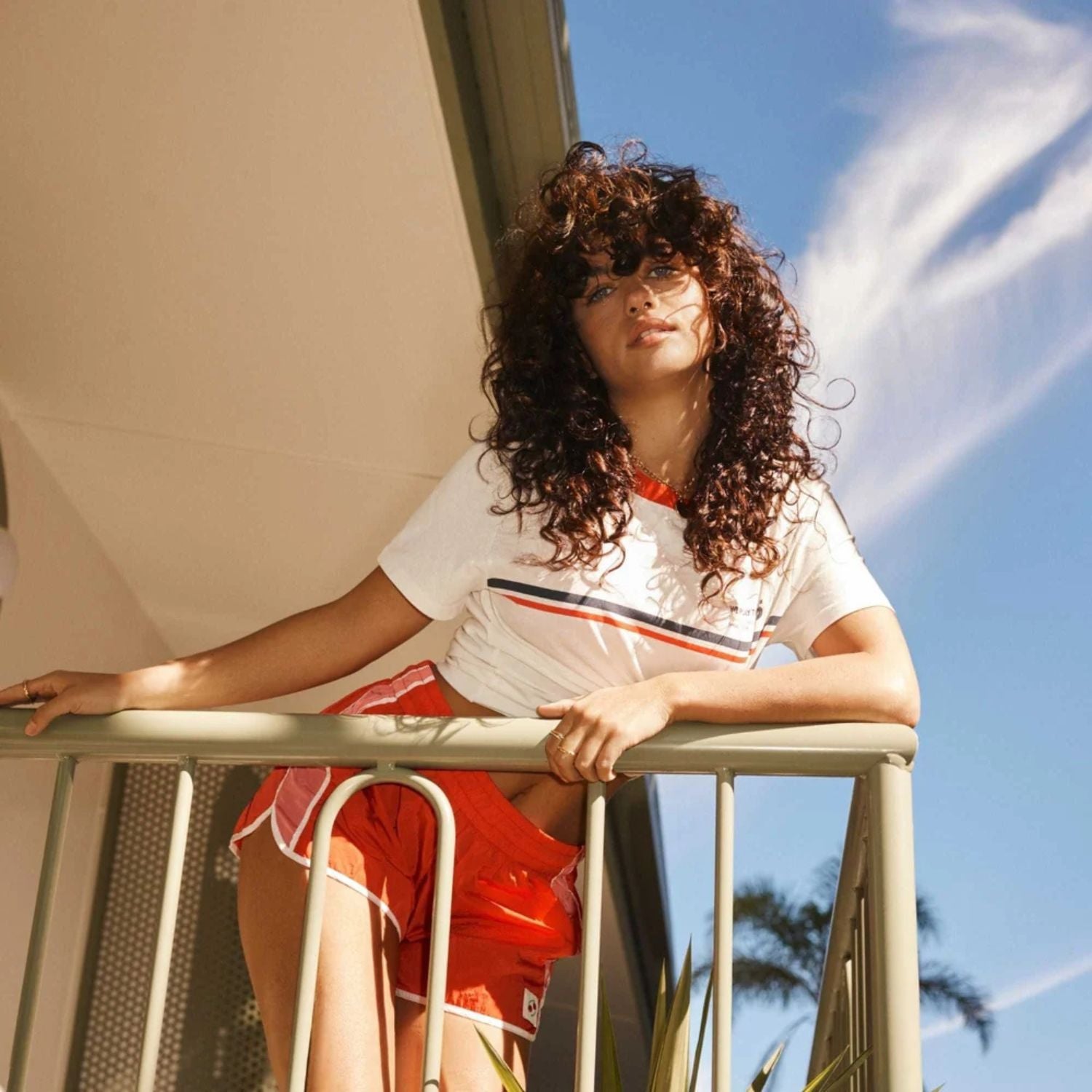 Woman standing on a balcony with a clear blue sky and some clouds in the background
