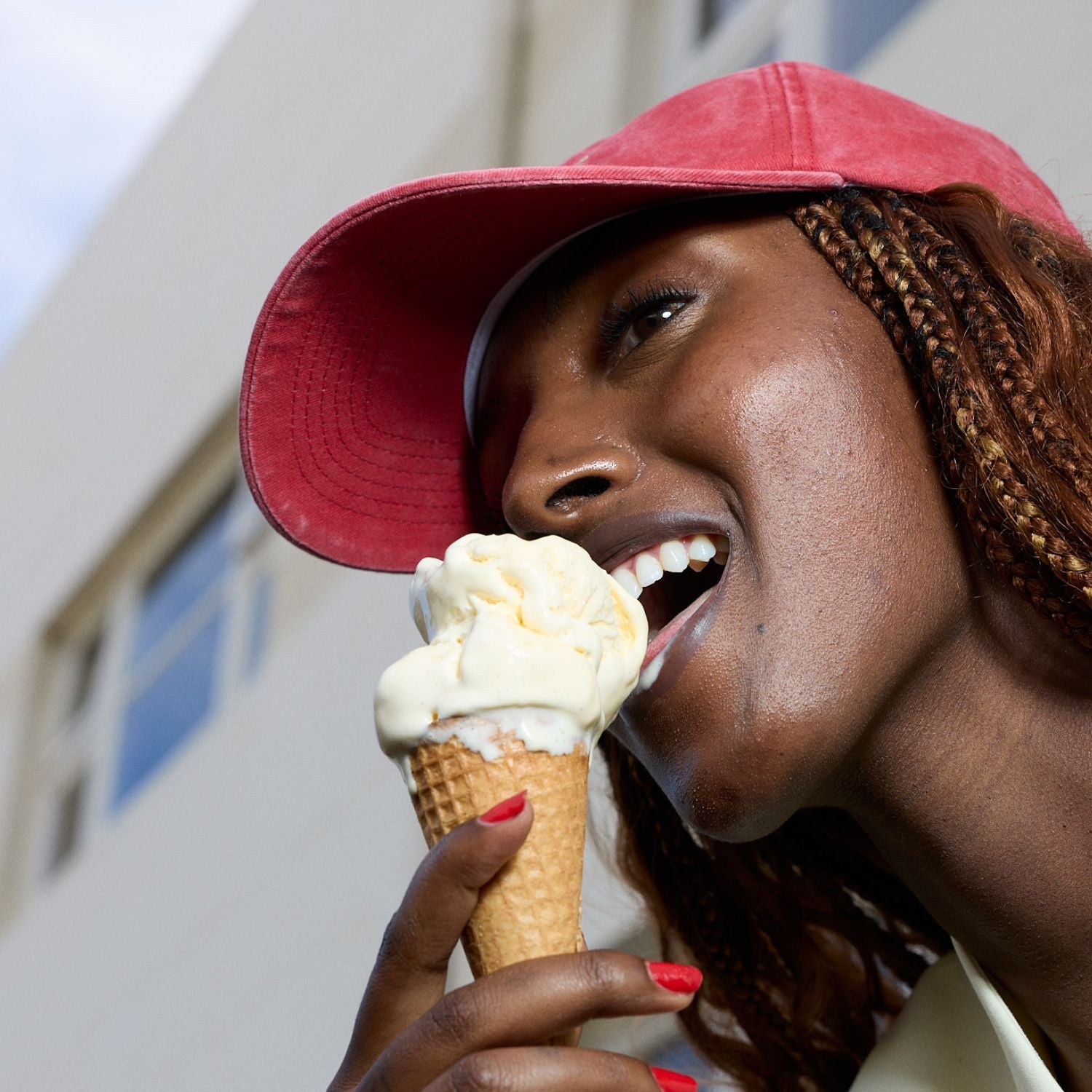 Person eating an ice cream cone with a red cap outdoors