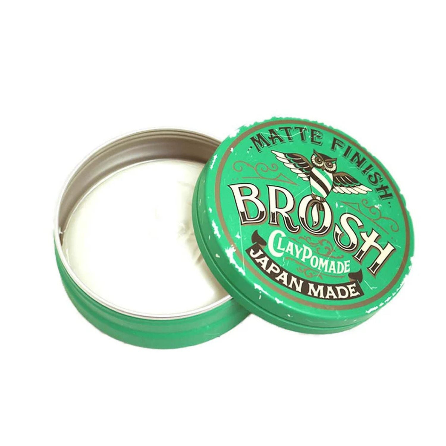 An open round metal tin of Brosh Clay Pomade with its lid leaning against it, showing the white pomade inside. The lid is bright green with white and gold text reading 'MATTE FINISH BROSH CLAYPOMADE JAPAN MADE'.