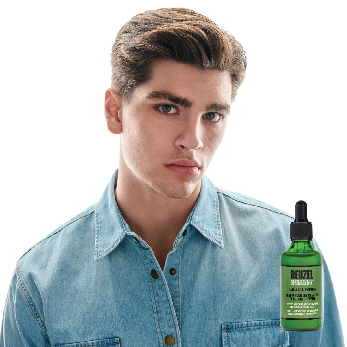 A young man with styled brown hair wearing a light blue denim shirt, shown against a white background with a green bottle of Reizel Hair & Scalp Serum positioned near his lower right.