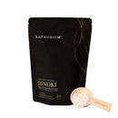 A black stand-up pouch of Bathorium Hinoki powder with a small wooden scoop filled with the light powder placed beside it on a white background.