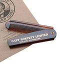 A vintage-style folding pocket comb with a dark wood handle and black metal teeth, featuring the text 'CAPT FAWCETT LIMITED' on the side. It is displayed diagonally on a brown kraft paper background with a circular logo stamp.