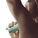 A close-up lifestyle shot of a man holding a light green cylindrical bottle under his arm, with a white background.
