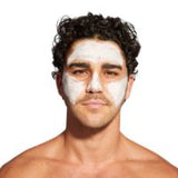 A close-up of a man with curly dark hair, showing white face mask on his forehead and cheek, against a plain white background.