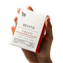A hand holding a white and orange box of DS Skincare Revita Tablets against a plain white background.