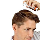 A man with styled brown hair using a hair spray bottle to style his hair, shown against a plain white background.