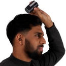 A man with a beard wearing a black long-sleeve shirt holds a black cylindrical hair product containing Nanogen hair powder to his head against a plain white background.