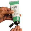 A hand holding a green and white tube of Baxter Beard Line Up Gel, with a small amount of gel dispensed onto a finger.